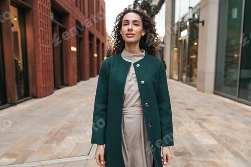 Preview: Portrait of young woman in green coat with curly hair in the city