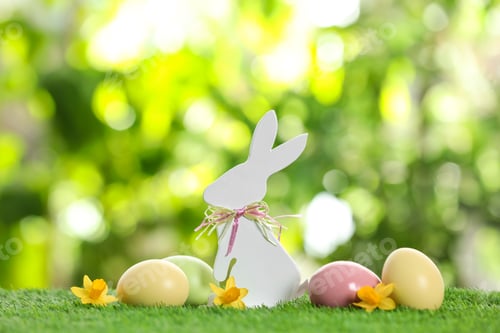 Preview: Cute wooden Easter bunny and dyed eggs on green grass against blurred background