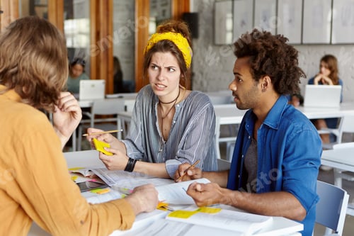 Preview: Pretty college student female with yellow scarf on head listening to her groupmates disagreeing with