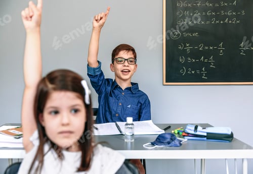 Preview: Students with mask on table raising hands at school