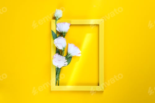 Preview: Yellow frame and flowers eustoma with a ray of sunshine on yellow background, copy space flat lay