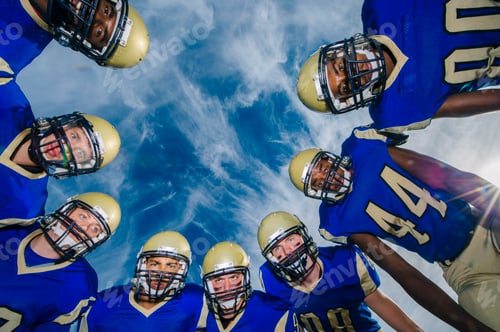 Preview: Low angle portrait of teenage and adult American football team against blue sky