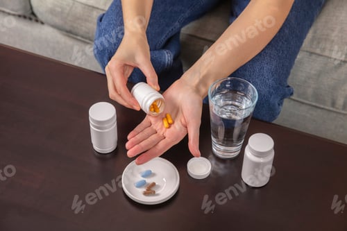 Preview: A woman takes vitamin supplements or medications at home while sitting on a sofa.