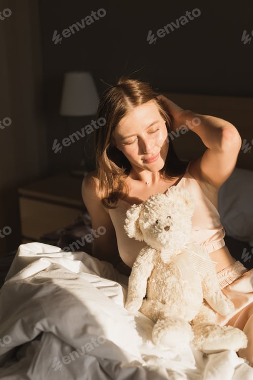 Preview: Portrait of girl is waking up in morning stretches in bed and sun shines from window. Happy young