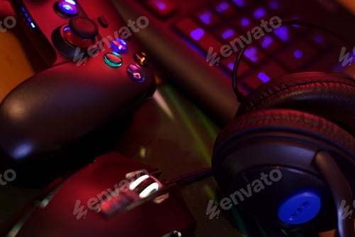 Preview: Modern gamepad and gaming mouse lies with keyboard and headphones on table in dark playroom scene