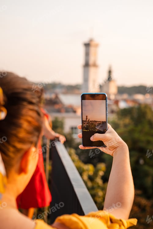Preview: Woman Tourist Looking At City On Sunset From Observation Deck Taking Picture On Her Phone