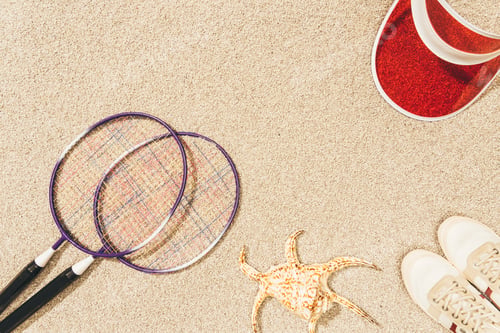 Preview: top view of arrangement of badminton equipment, cap and shoes on sand