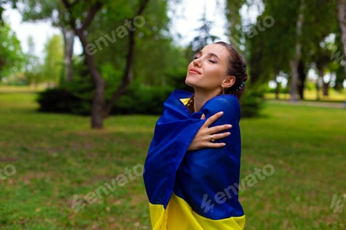 Preview: young ukrainian woman stands with the flag of ukraine in nature