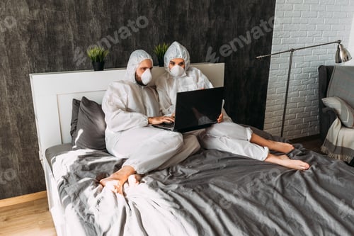 Preview: Couple in Hazmat Suits Using Laptop in Bed