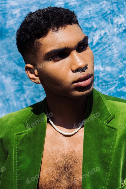 Preview: portrait of stylish african american man in piercing looking away near blue drape on background