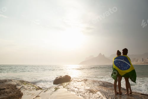 Preview: Rear view of two young women wrapped in Brazilian flag on Ipanema beach, Rio De Janeiro, Brazil