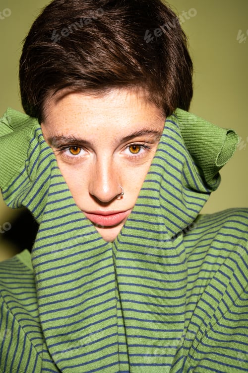 Preview: portrait of pensive freckled woman in striped pullover looking at camera on green background