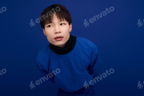 Preview: Captivating young asian man poses confidently against a vibrant blue backdrop