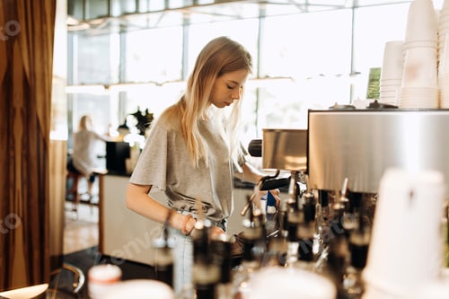 Preview: A young pretty thin blonde,dressed in casual outfit,is cooking coffee in a popular coffee shop
