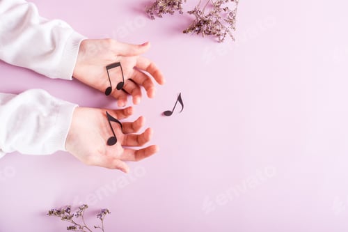 Preview: Children's hands hold paper notes on a pink background. Music education. Top view.