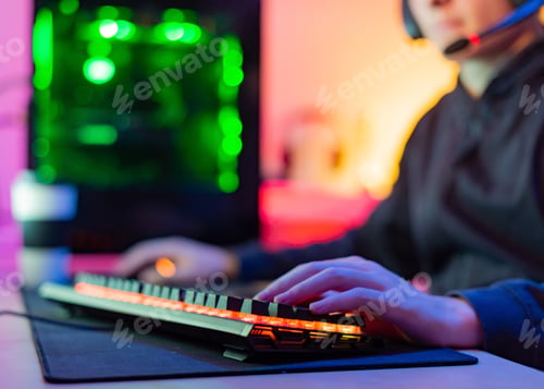Preview: Unrecognizable young gamer with hands on illuminated keyboard in room with colored background