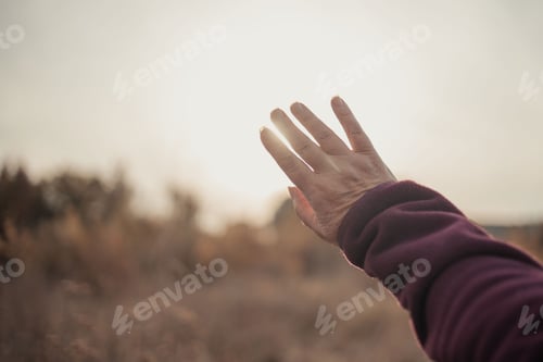Preview: Female hand reaches for bright sunlight during sunset