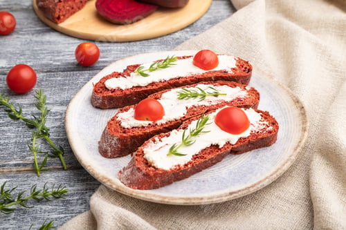 Preview: Red beet bread sandwiches with cream cheese and tomatoes on gray wooden background. Side view.