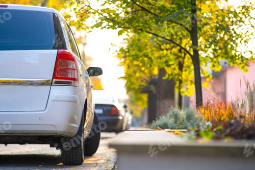 Preview: Cars parked in a row on a city street side on bright autumn day.