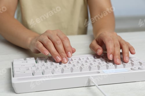 Preview: Woman typing on modern keyboard with RGB lighting at white wooden table, closeup