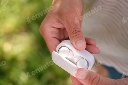Preview: Woman hand open a case with wireless headphones, outdoors