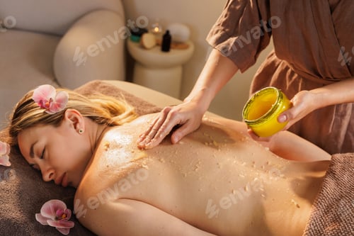 Preview: Therapist massages exfoliating scrub into woman's back during spa skincare treatment.
