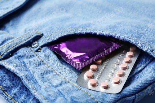 Preview: Purple condom and birth control pills in pocket of jeans, closeup. Safe sex concept