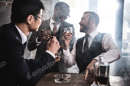 Preview: Multiethnic group of businessmen smoking and drinking whisky indoors, multicultural business team