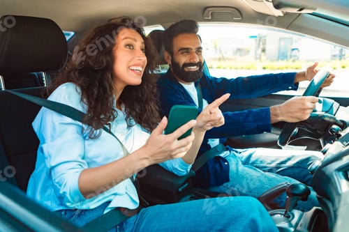 Preview: Happy middle eastern couple driving using cellphone gps app, woman passenger showing way to driver