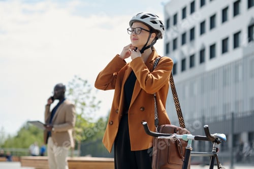 Preview: Happy young female employee fastening belt of protective cycling helmet