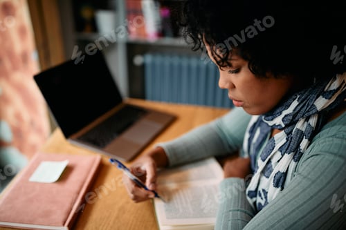 Preview: Mid adult African American woman reading while studying in a library.