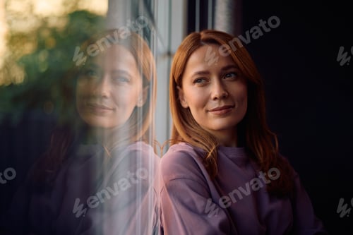 Preview: Smiling woman day dreaming while leaning on a window.