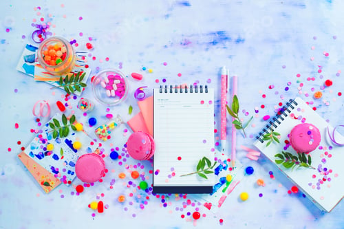 Preview: Planning a party concept with confetti, pink macarons, candies and an open notepad with blank pages