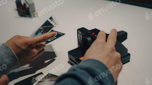Preview: Close-up shot of hands holding an instant camera and printed pictures