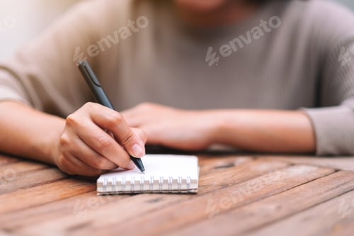 Preview: Closeup image of a woman writing on blank notebook on wooden table