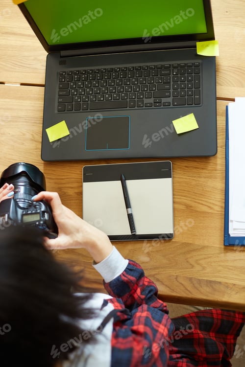 Preview: Photographer female working in a creative office holding camera, at desk and retouch photo