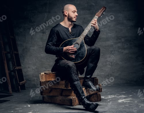 Preview: Traditional folk musician dressed in vintage Celtic clothes sits on a wooden box and plays mandolin.