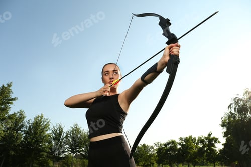 Preview: Woman with bow and arrow practicing archery outdoors, low angle view