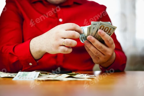 Preview: closeup of male hands counting a stack of US one hundred dollar bills