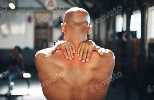 Preview: Rearview shot of a muscular young man experiencing back pain while exercising in a gym