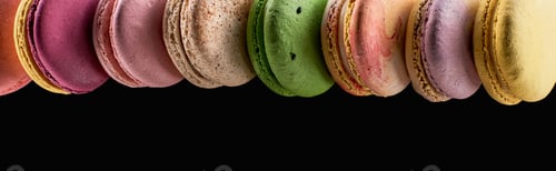 Preview: row of tasty colorful French macaroons of different flavors isolated on black with copy space,