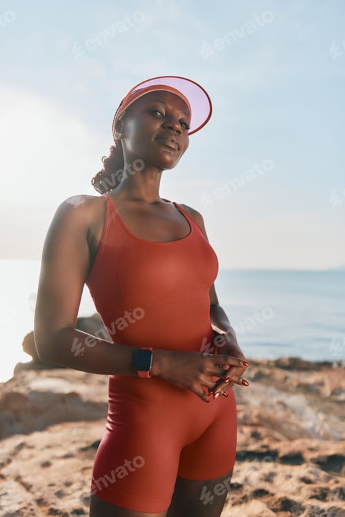 Preview: Confident woman in a red sports outfit standing by the beach during sunset Soft ocean waves in the