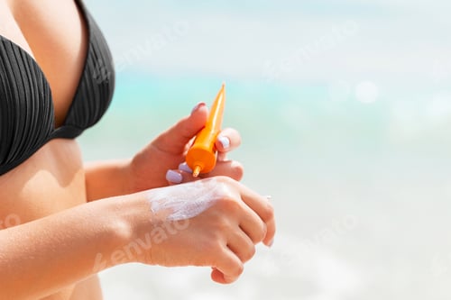 Preview: Tanned girl is using sunscreen on her hand at the beach