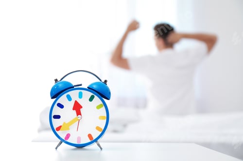 Preview: Analog alarm clock and blurred man on background. Time of day