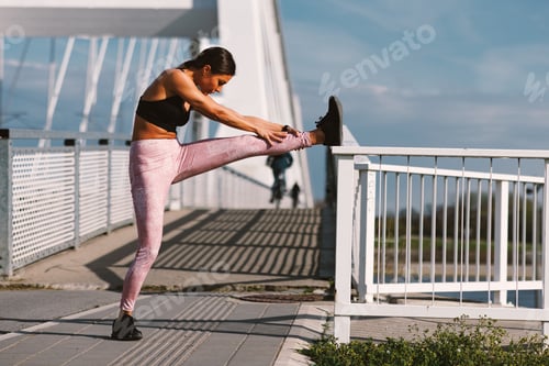 Preview: Young fitness woman stretches before jogging on a bridge in the city