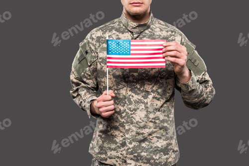 Preview: cropped view of soldier in uniform holding american flag isolated on grey