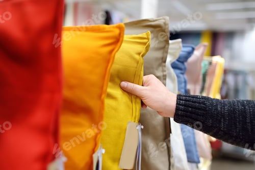 Preview: Man choices pillow in shop. Variety of colour pillows on shopping stand in supermarket