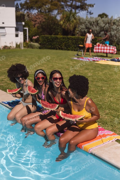 Preview: Diverse group of female friends eating watermelon sitting at the poolside talking
