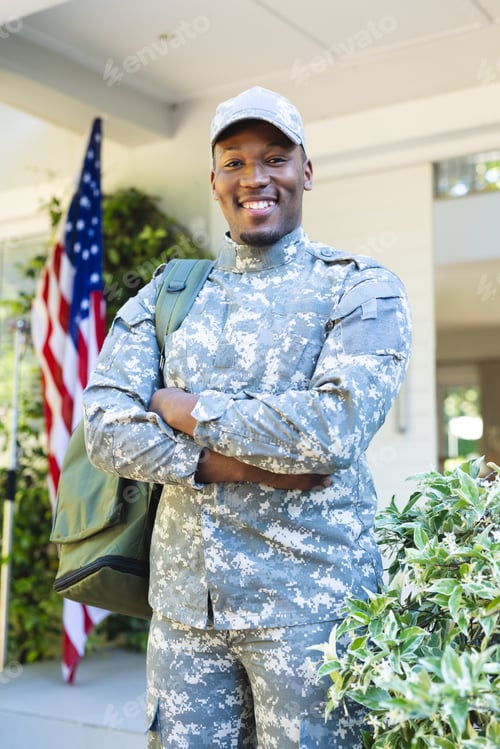 Preview: Happy african american male soldier with arms crossed in cap outside home with usa flag, copy space