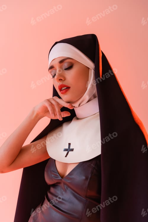 Preview: sexy nun touching face while posing with closed eyes isolated on pink